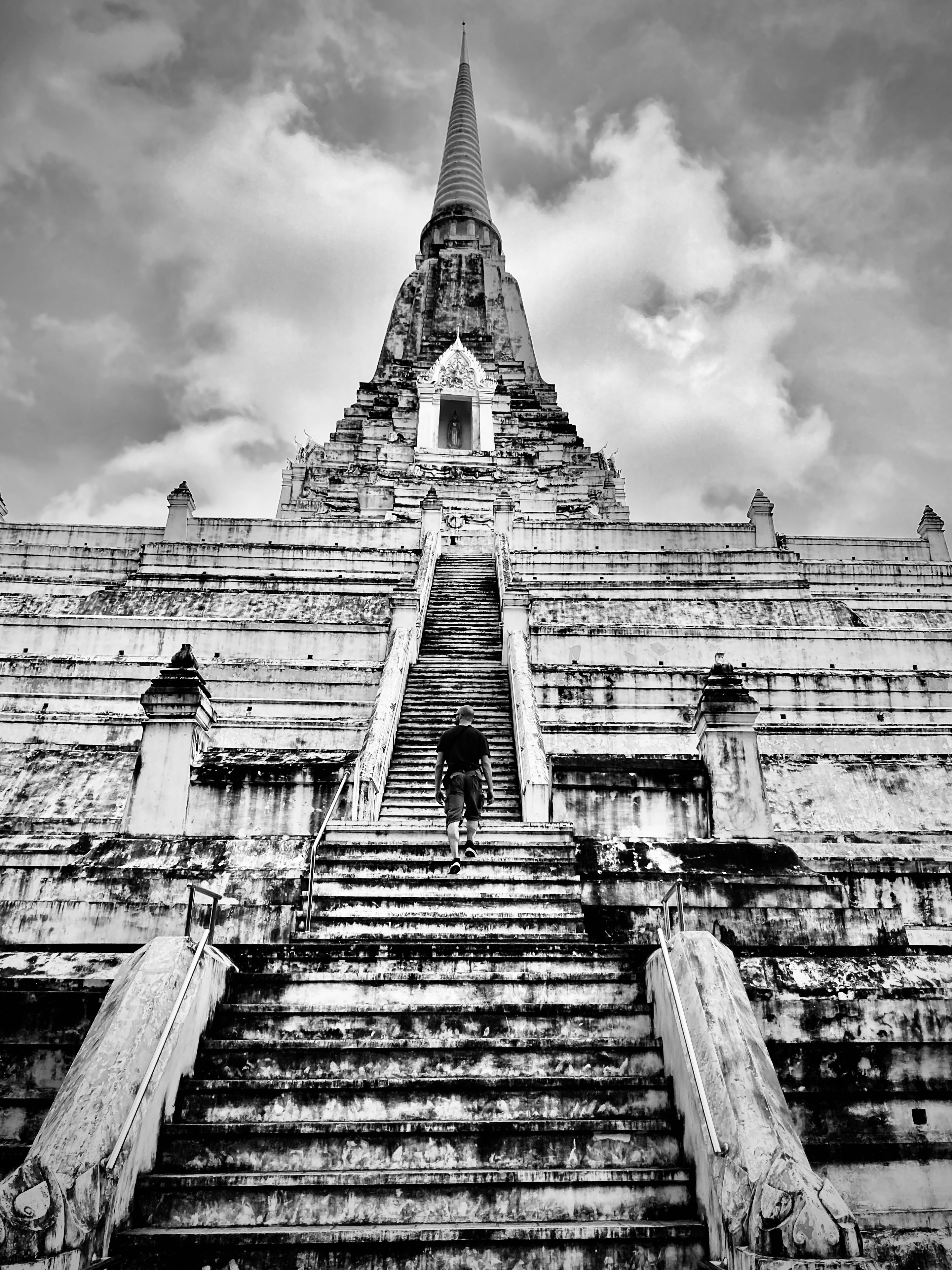 scalinata ripida verso uno stupa alto ad Ayutthaya: pietra bianca consunta, cielo nuvoloso drammatico, figura in salita
